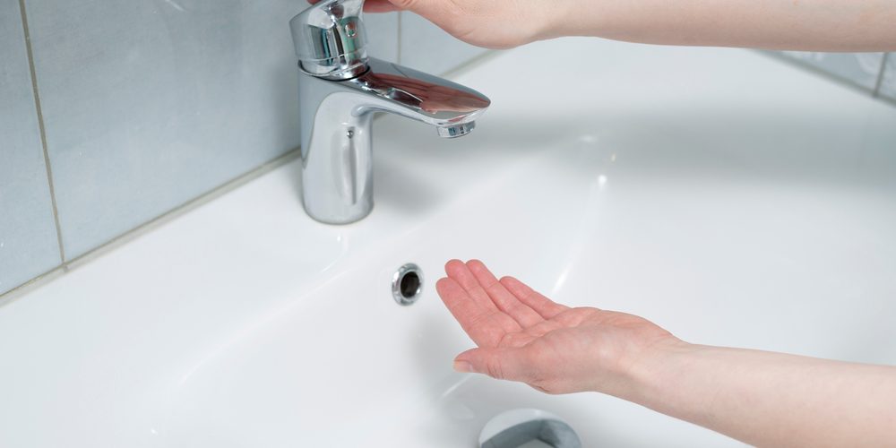 A woman attempts to use her bathroom sink by turning on the faucet.