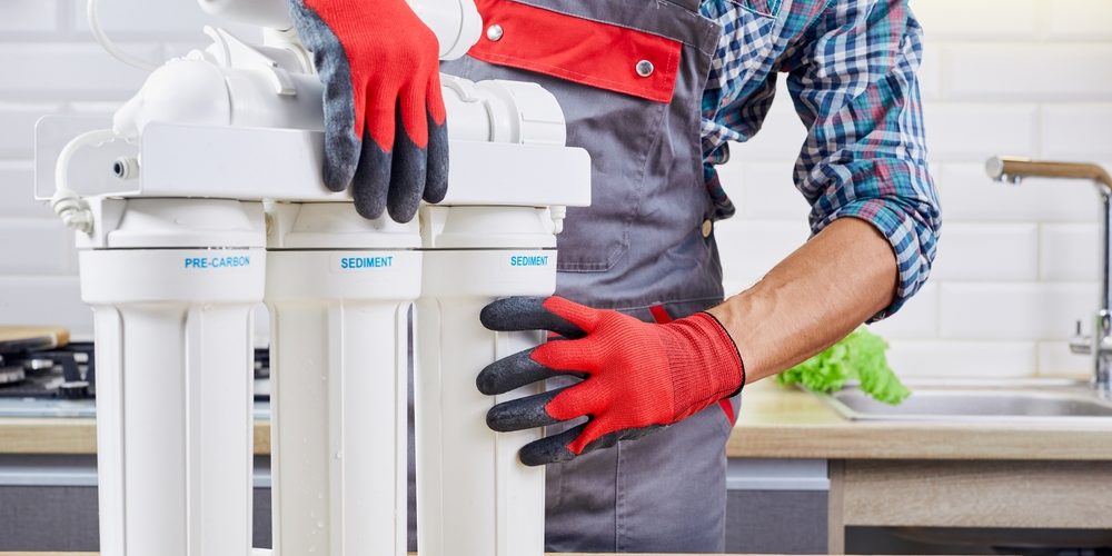 A plumber with several water filter pipes gets ready to install them in the sink behind him