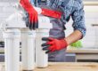 A plumber with several water filter pipes gets ready to install them in the sink behind him