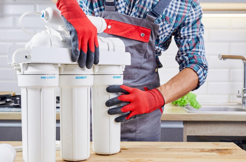 A plumber with several water filter pipes gets ready to install them in the sink behind him