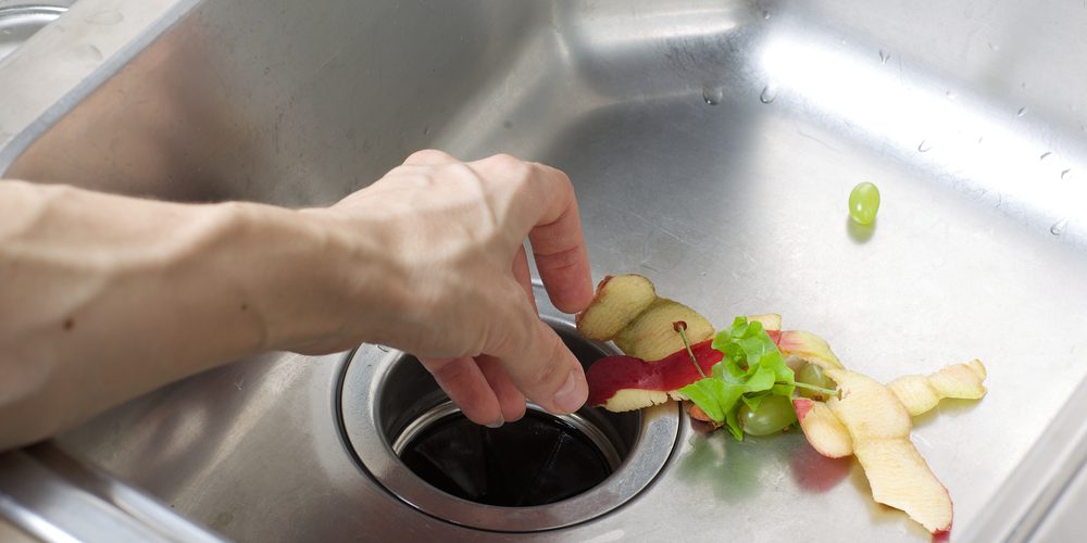 A person puts leftover food through their kitchen sink's garbage disposal