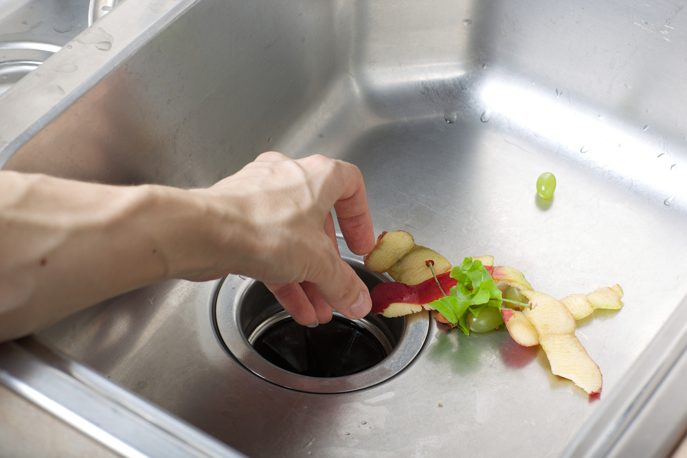 A person puts leftover food through their kitchen sink's garbage disposal