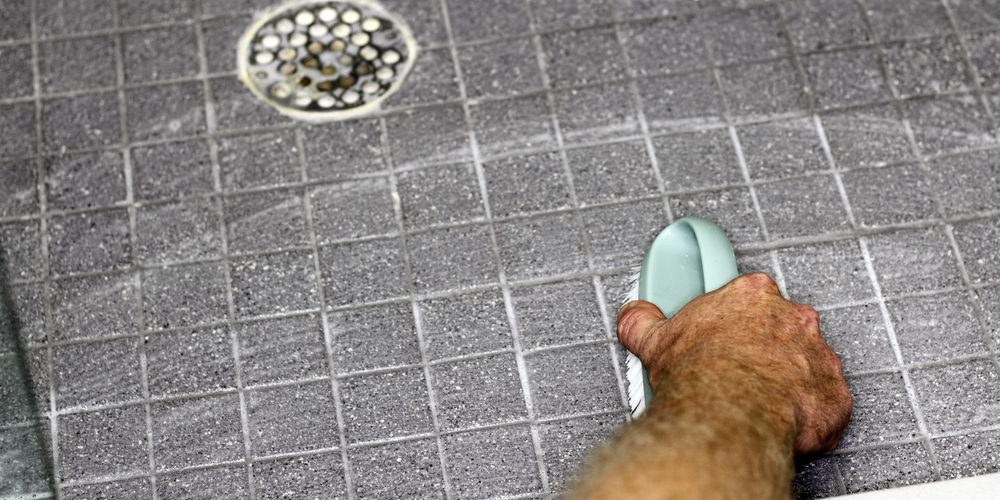 A person uses a sponge to scrub down the floor near a shower drain