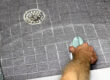 A person uses a sponge to scrub down the floor near a shower drain