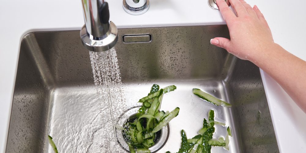 A close up of food waste being put into a garbage disposal