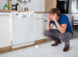 A man looks on in shock as soap emerges from the closed dishwasher in front of him