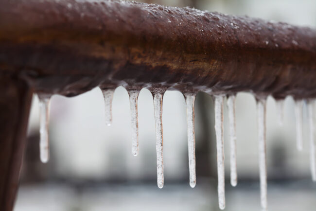 Icicles,Hanging,From,A,Brown,Pipe.,Frozen,Water,And,Metal A closeup of a frozen brown pipe